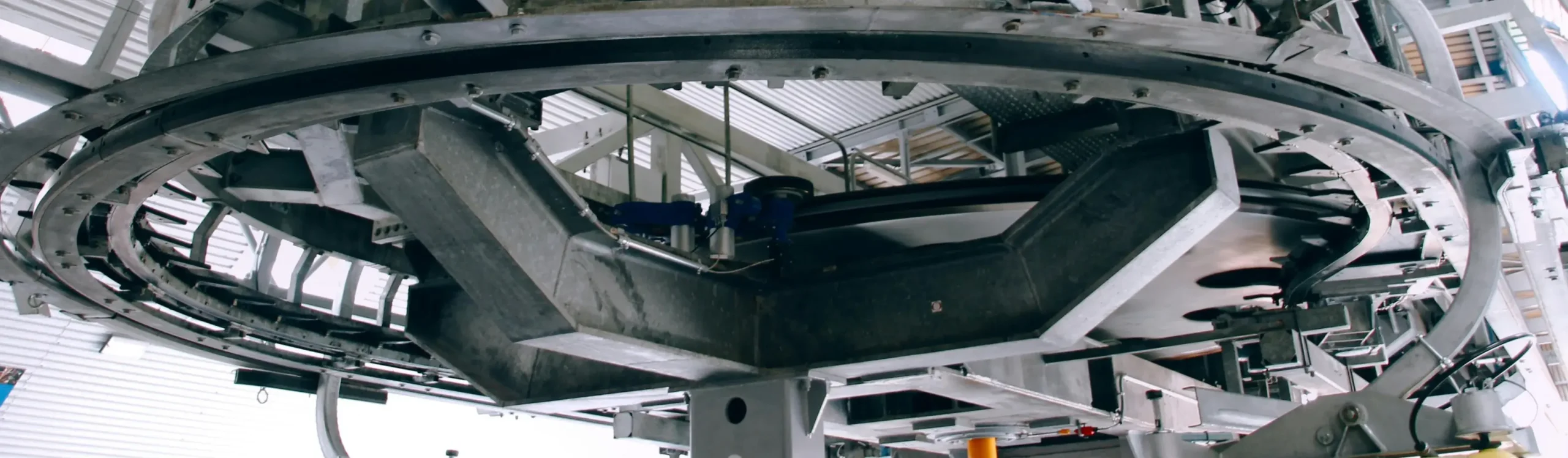 A low-angle shot of a heavy-duty circular steel conveyor rail and structural support beams inside a large manufacturing plant.