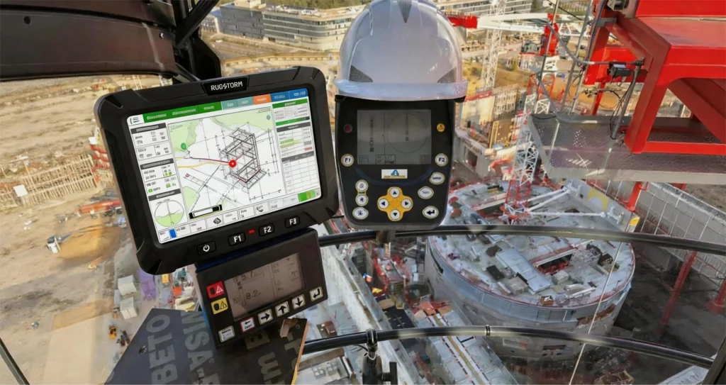 Interior view of a construction crane operator's cabin featuring a Rugstorm vehicle display displaying 3D building schematics and digital control interfaces overlooking a large construction site.